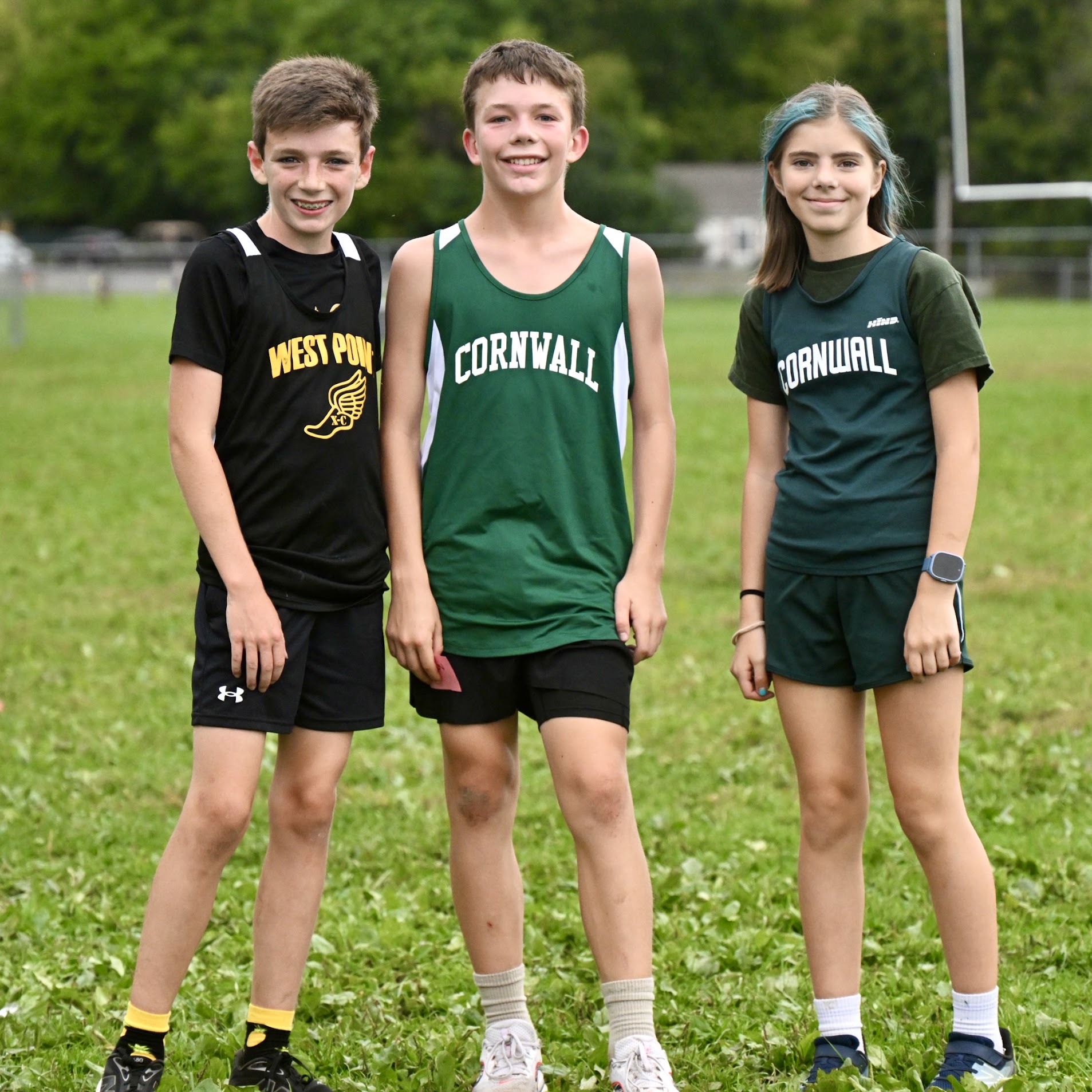 Cal and two friends in cross country uniforms standing together on a grass field after a meet.